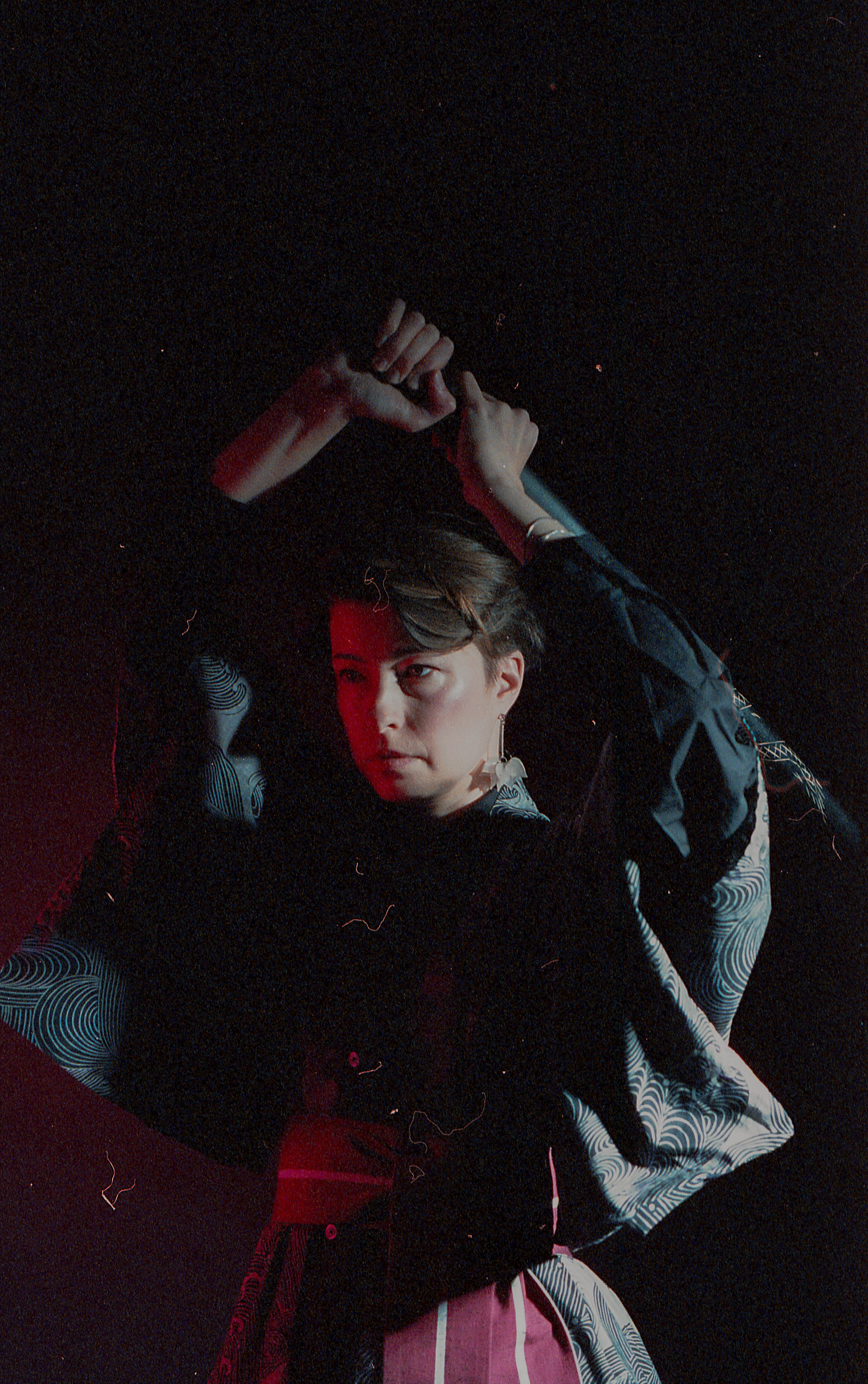 Yulia in deep red light, blade drawn behind her shoulders